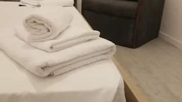 A neatly made bed with folded white towels, a dark armchair, and a wooden nightstand.