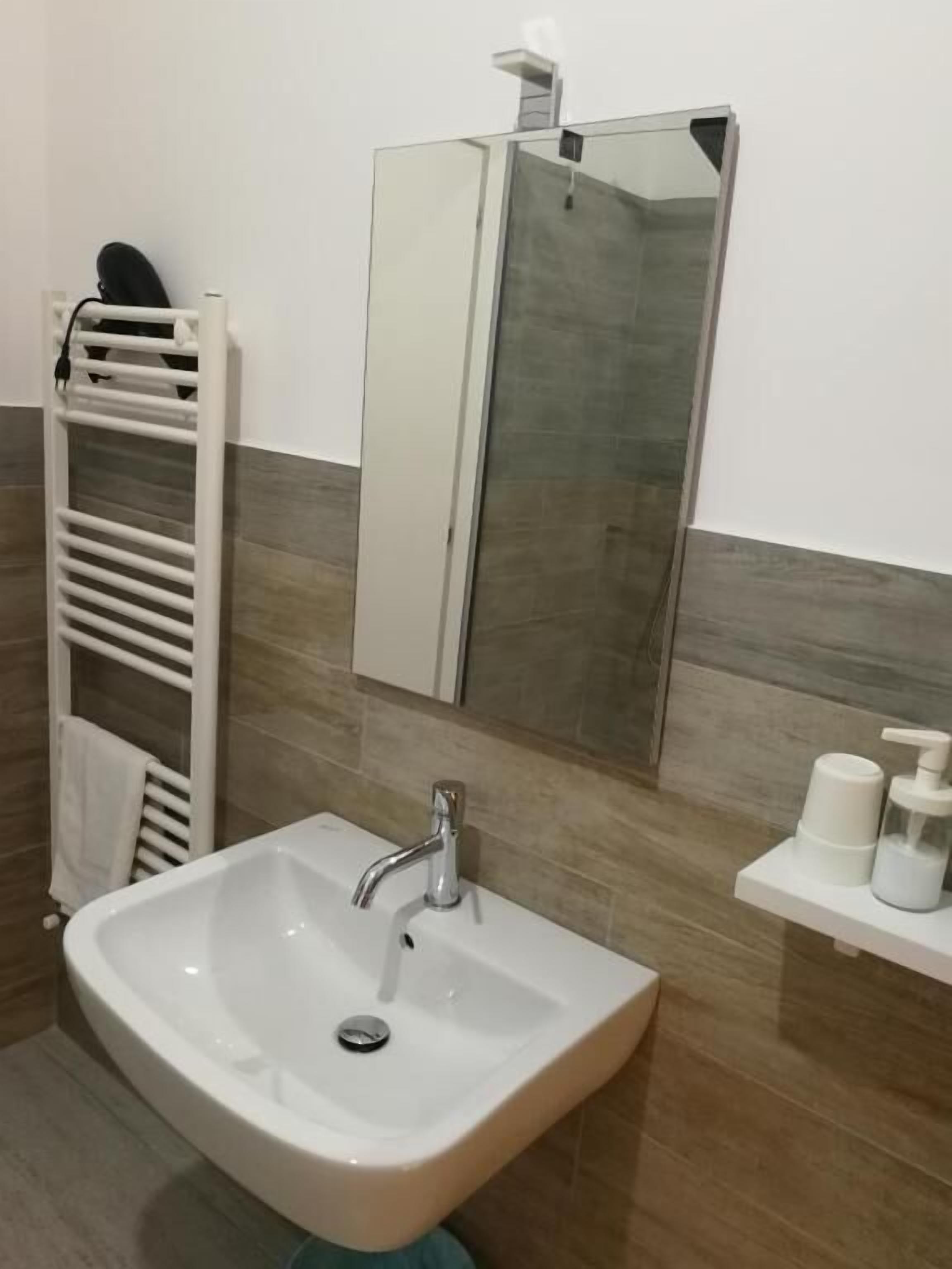 Ein Badezimmer mit einem weißen Waschbecken, einem Spiegel, einem Handtuchhalter und einem Seifenspender auf einem Regal.