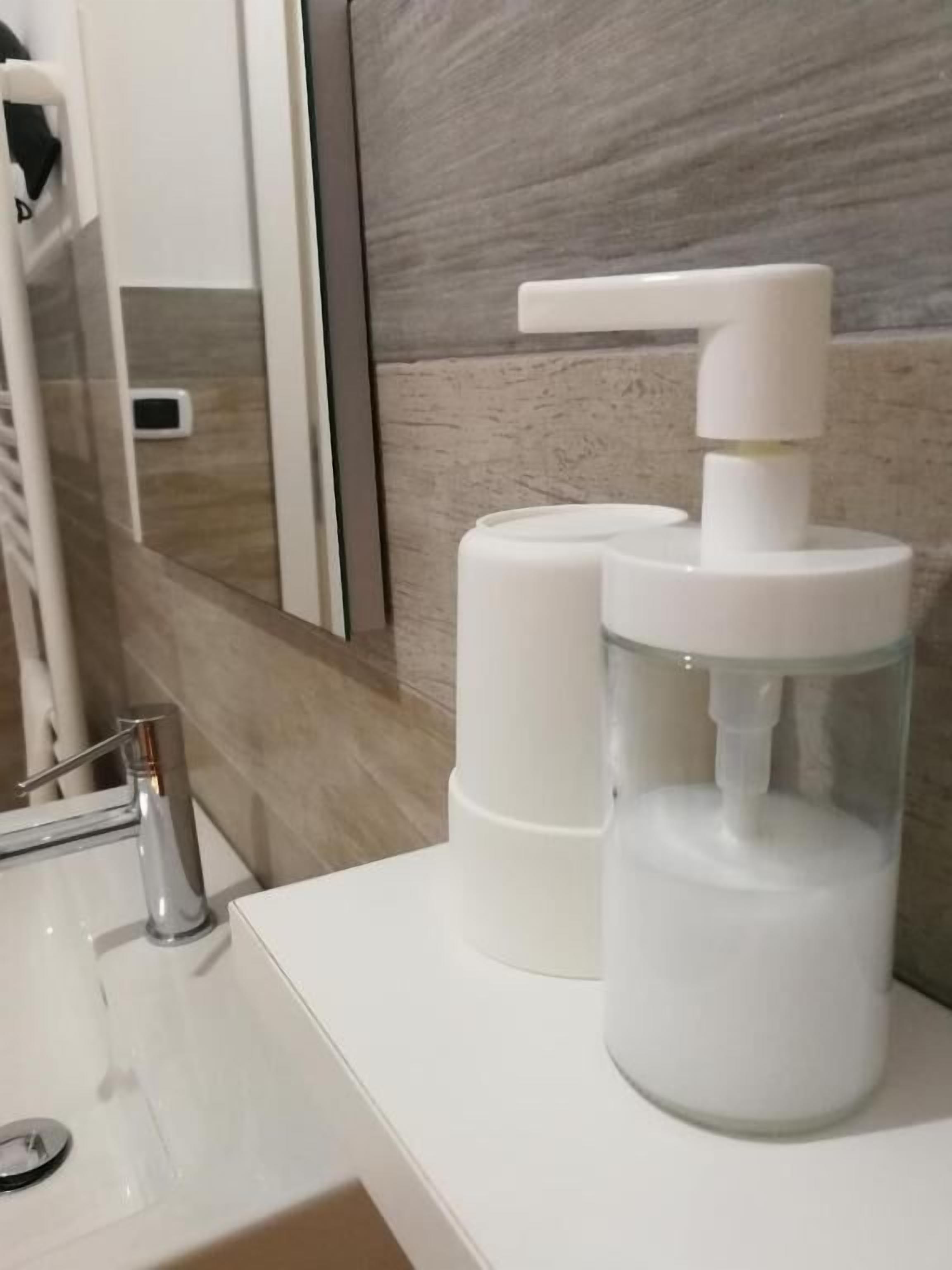 A bathroom with a white sink, a mirror, and a soap dispenser.