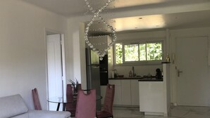 En moderne stue med et glasbord, en hvid sofa og et spiseområde med en lysekrone.