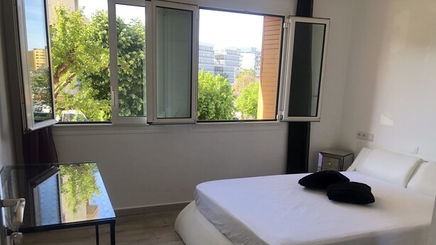 Et moderne hotelværelse med en stor seng, et lille natbord og et vindue med udsigt over byen.