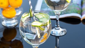 Two glasses of a clear beverage with lime slices and a straw, placed on a reflective surface with an open book and oranges in the background. - Stunning 1-bed Cottage Near Carlisle With Hot tub (Carlisle)