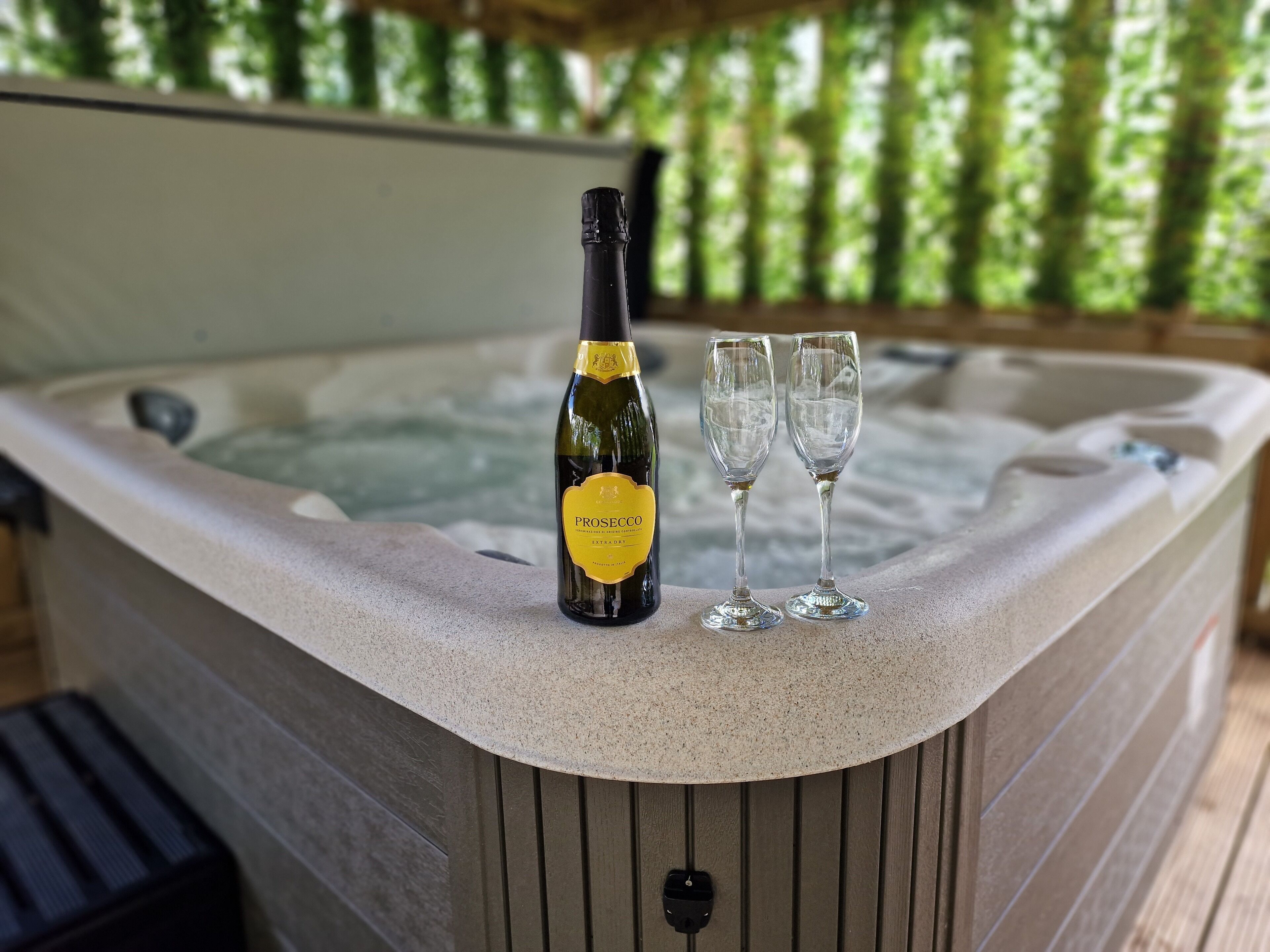 Un bain à remous avec une bouteille de prosecco et deux verres posés sur le bord.