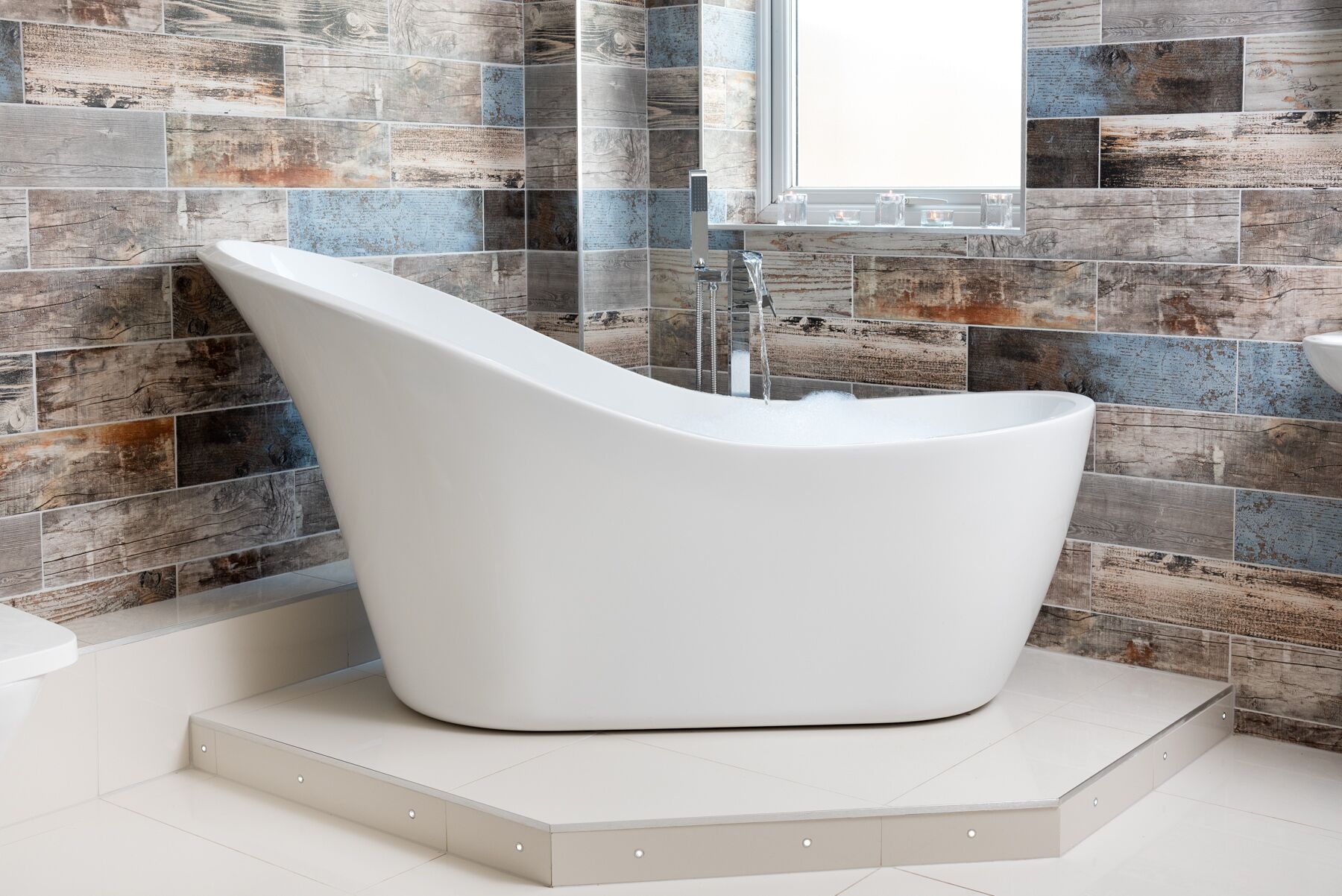 A modern bathroom with a freestanding bathtub, a window, and a rustic wall design.
