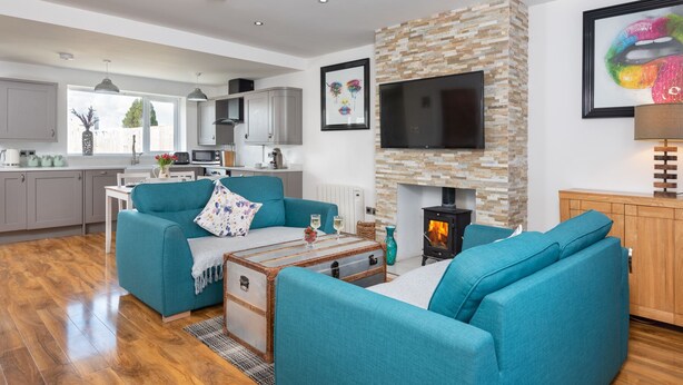 A modern living room with teal sofas, a fireplace, a TV, and a kitchen in the background. - Stunning 1-bed Cottage Near Carlisle With Hot tub (Carlisle)