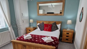 A bedroom with a wooden bed, two bedside tables, a mirror, and a radiator. - Stunning 1-bed Cottage Near Carlisle With Hot tub (Carlisle)