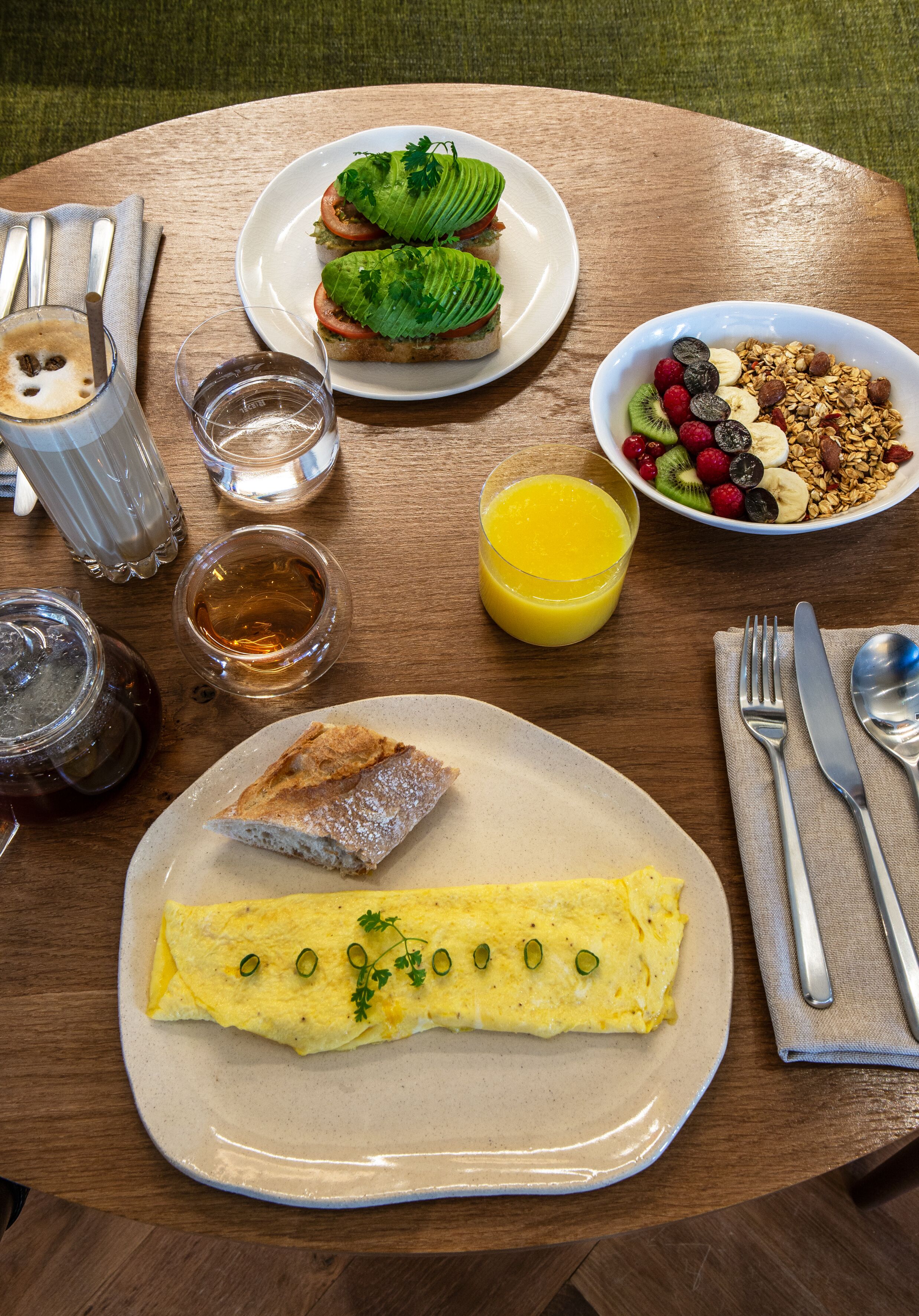 Una mesa de desayuno con huevos, un sándwich, un cuenco de fruta, un vaso de jugo y una taza de té.