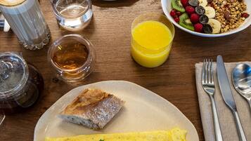 Una mesa de desayuno con huevos, un sándwich, un cuenco de fruta, un vaso de jugo y una taza de té.