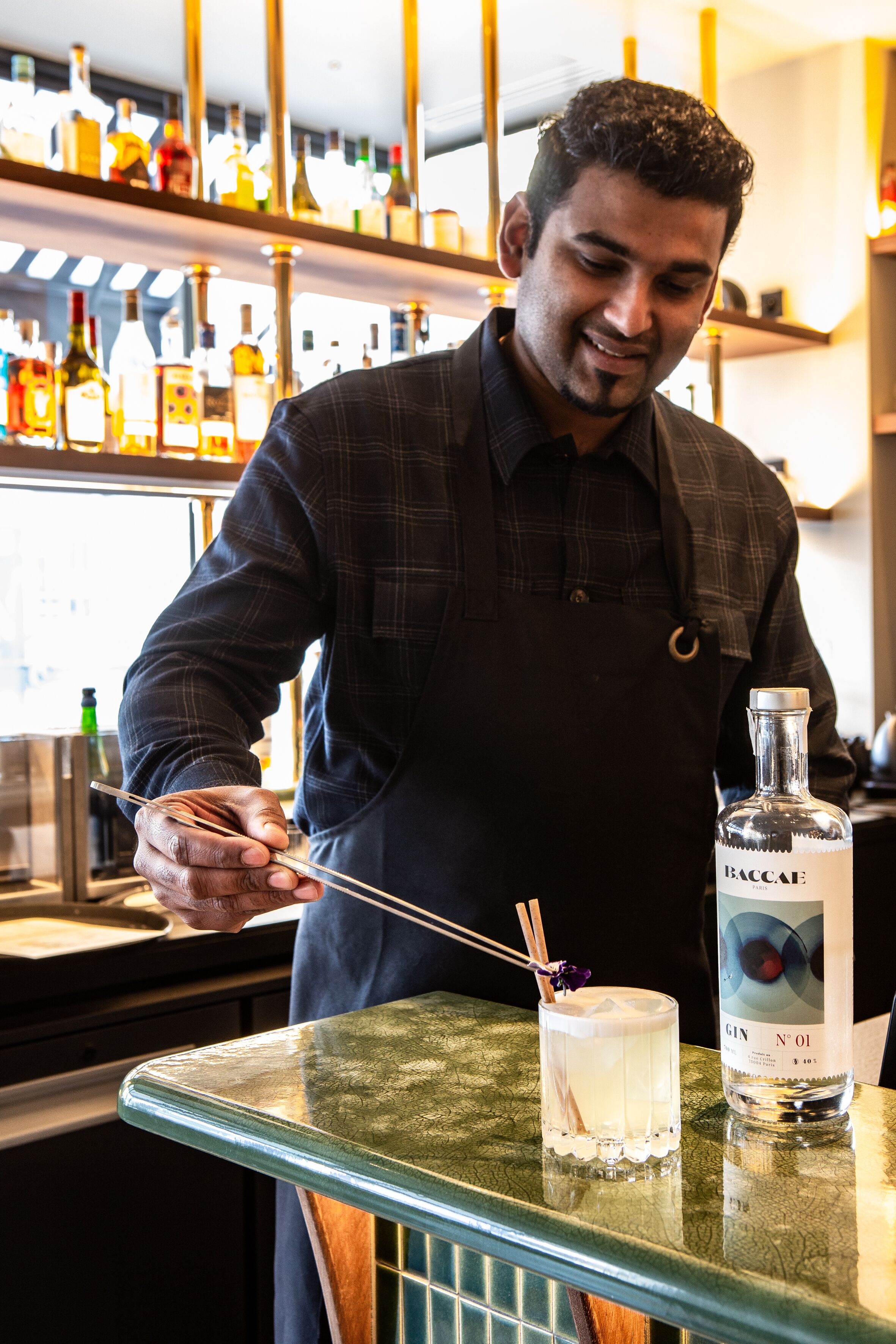 A bartender preparing a drink with a bottle of Baccae Gin N'O1 on the counter.