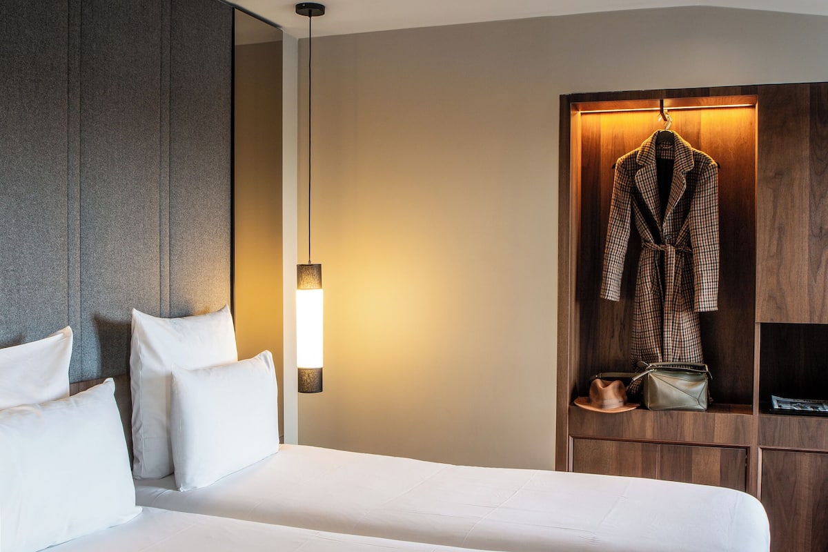 A hotel room with a large bed, a robe hanging on a wooden rack, and a small table with a handbag and a hat.