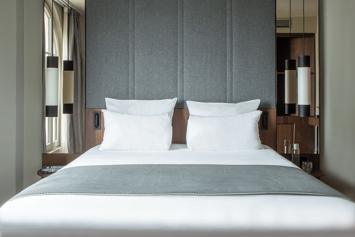 A modern hotel room with a large bed, grey headboard, and a mirror on the wall.
