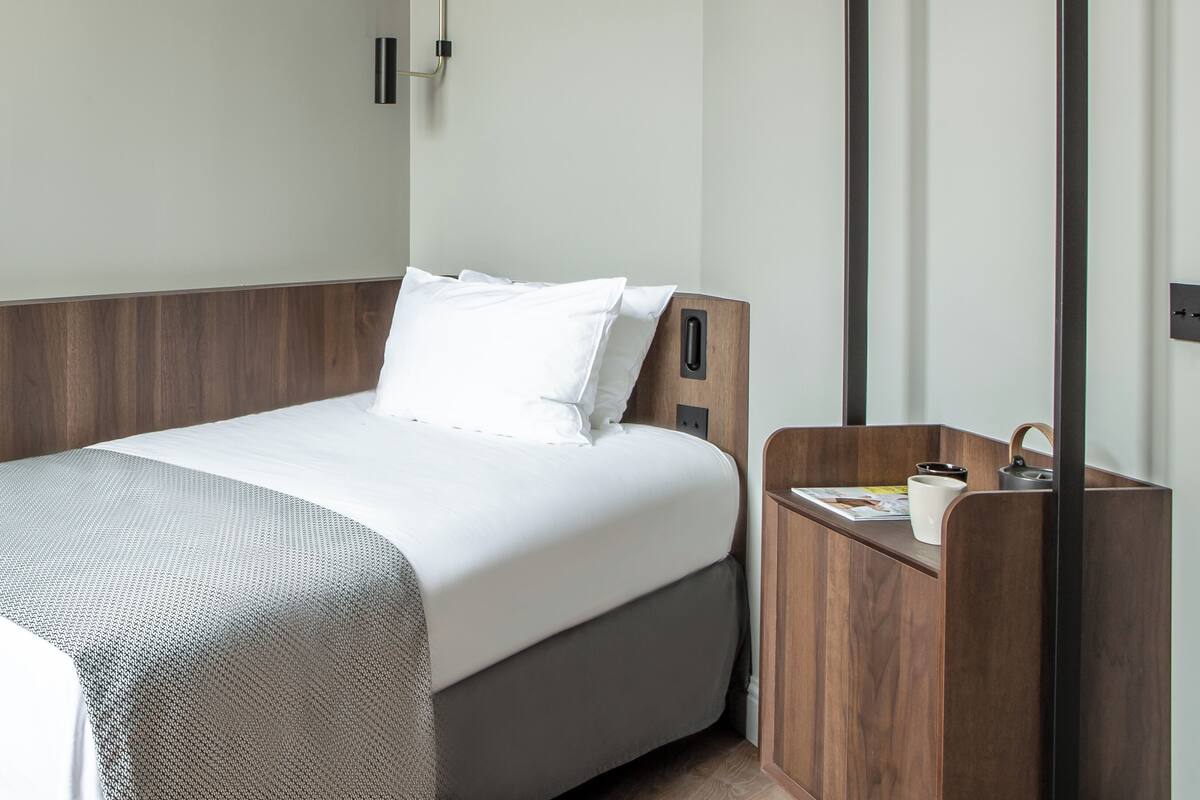 A modern hotel room with a large bed, a wooden nightstand, a built-in wardrobe, and a wall-mounted towel rack.