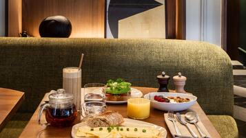 A cozy dining area with a wooden table set for breakfast, including a teapot, a glass of juice, and a plate of food.