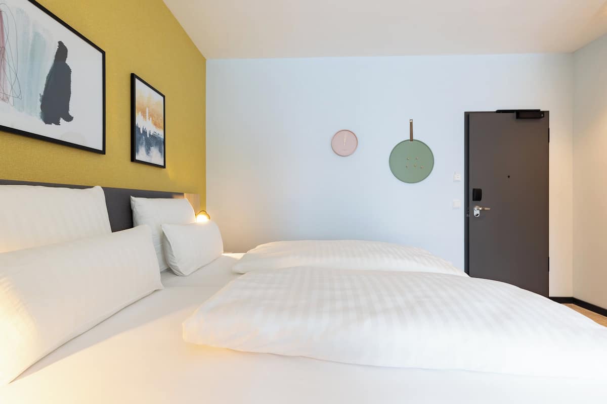 Ein Hotelzimmer mit einem Bett, einem Nachttisch, einer Wanduhr und einer Tür.