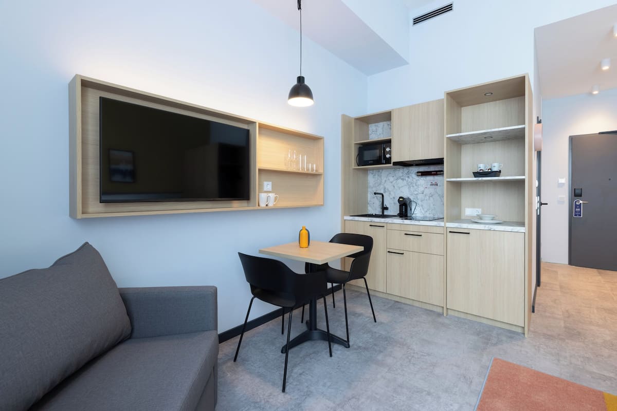 Ein kompakter Wohnbereich mit Sofa, Esstisch, Stühlen, Fernseher, Küchenzeile und einer Tür.