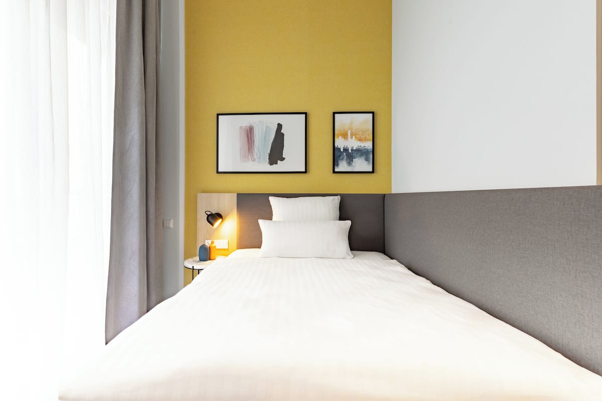 Ein Hotelzimmer mit Bett, Nachttisch mit Lampe und zwei gerahmten Kunstwerken an der Wand.