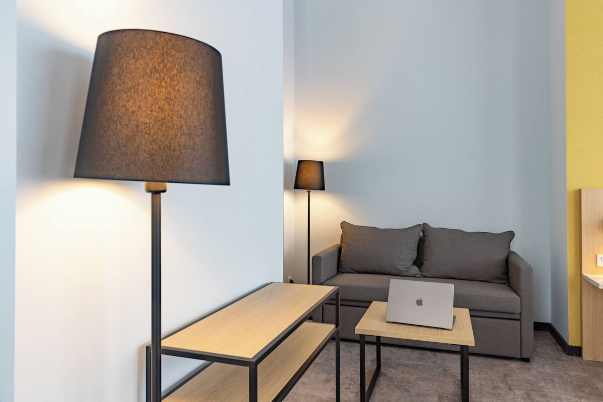A modern room with a sofa, a desk with a laptop, and two lamps.