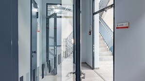 A modern hotel corridor with glass doors, a staircase, and an elevator sign.
