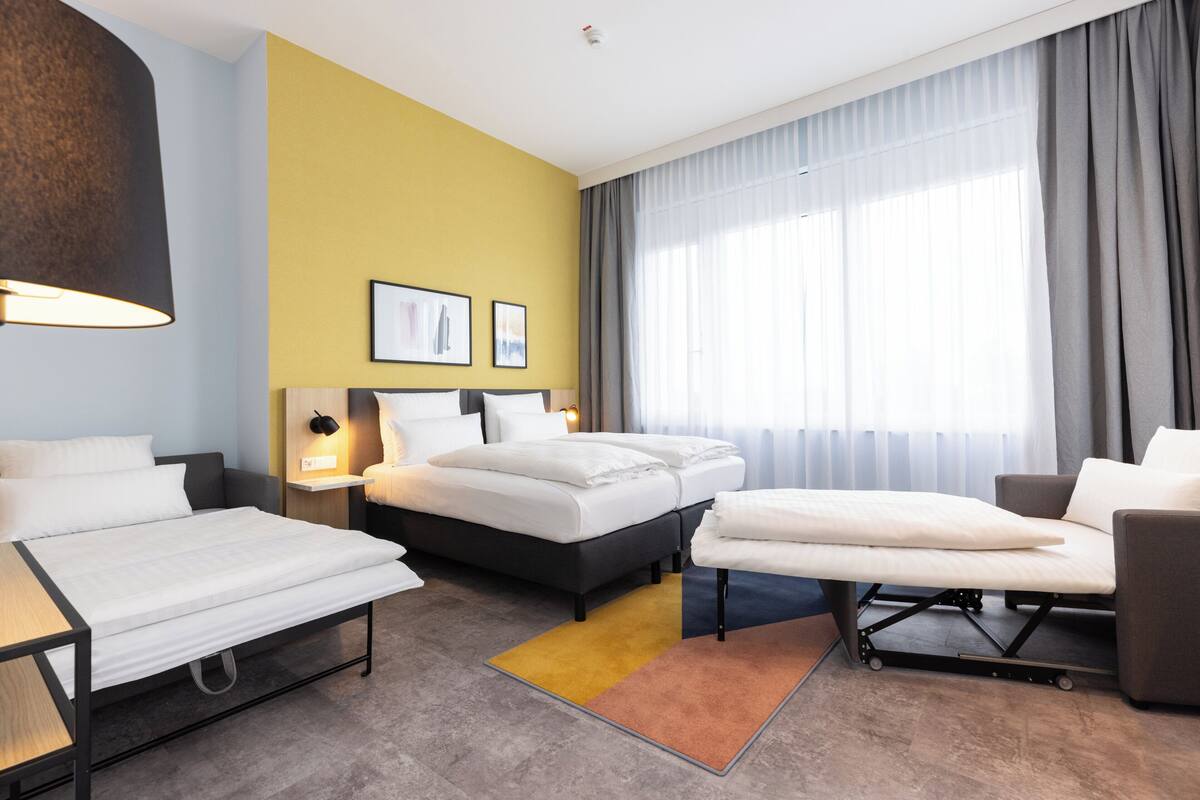 A hotel room with two beds, a sofa, a desk, a lamp, and a window with curtains.