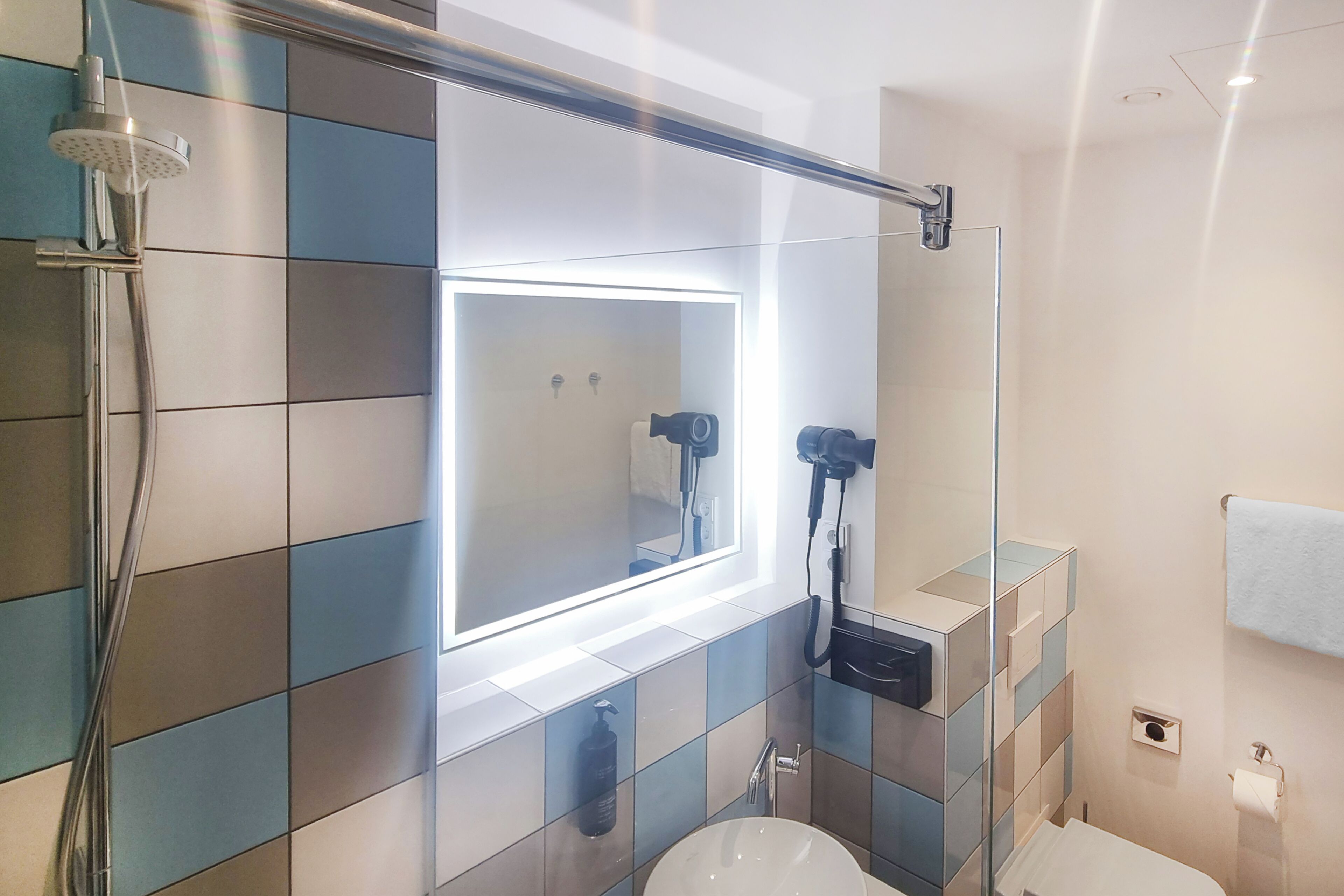 Un baño moderno con cabina de ducha de vidrio, un espejo grande con iluminación integrada y un inodoro.