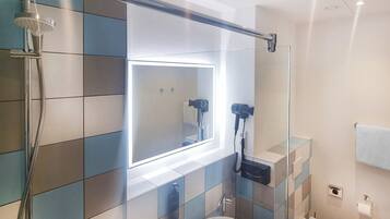 Un baño moderno con cabina de ducha de vidrio, un espejo grande con iluminación integrada y un inodoro.