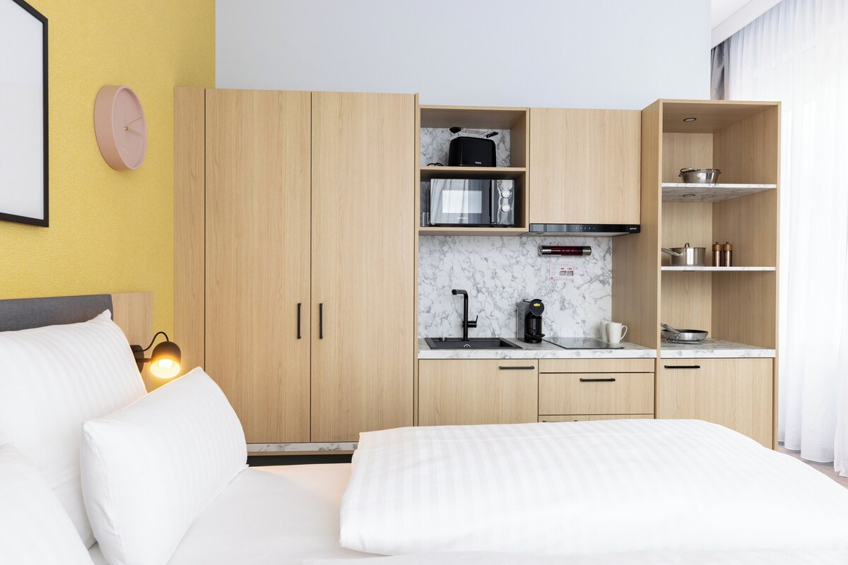 Een hotelkamer met een bed, een klein keukentje met een magnetron, een koffiezetapparaat en een wastafel.