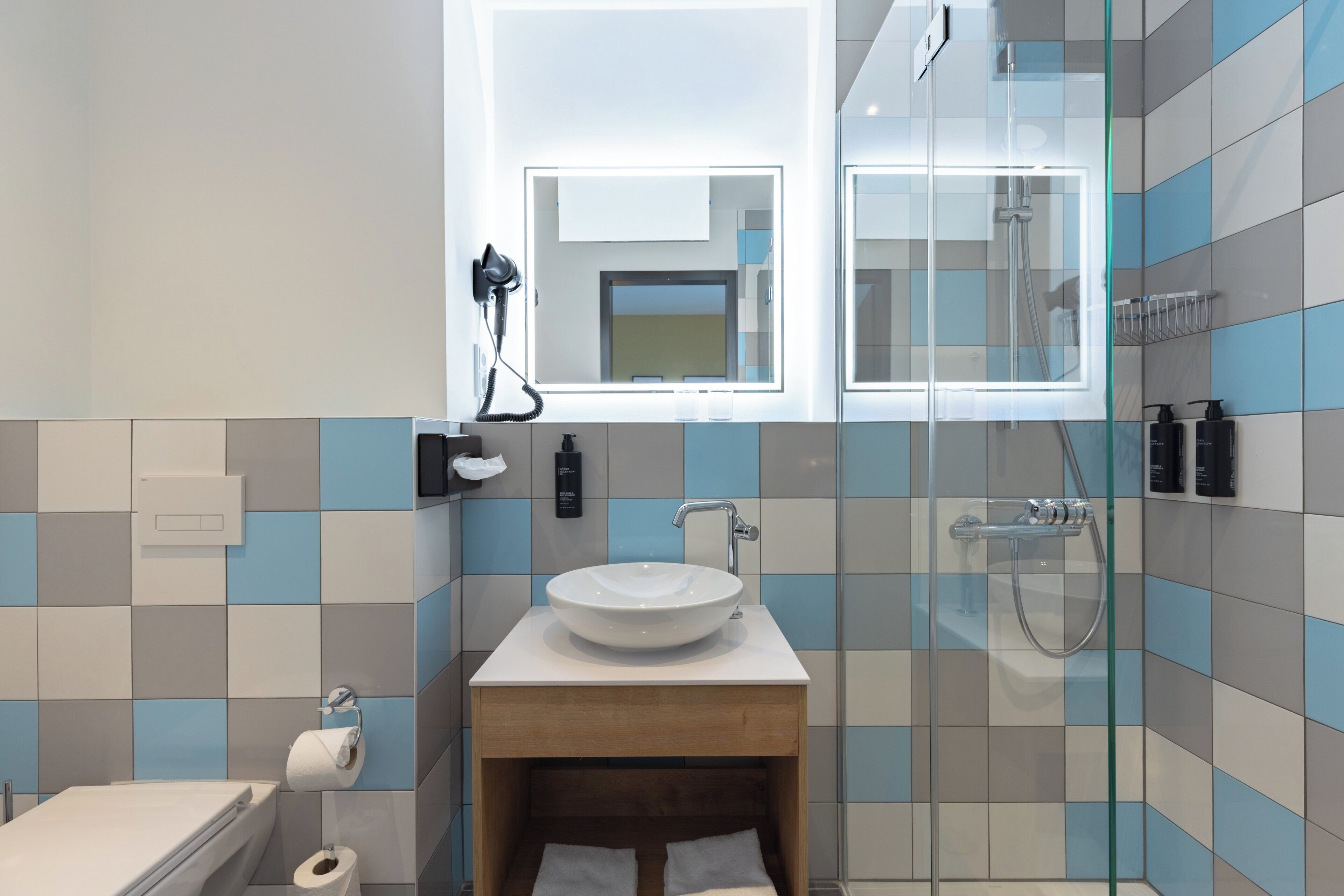 Un baño moderno con cabina de ducha de vidrio, un lavamanos blanco y un mueble de tocador de madera.