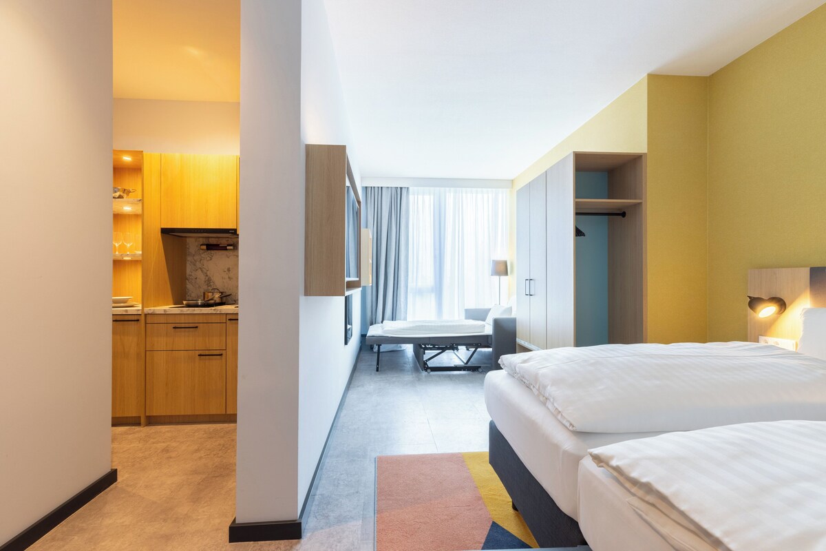 Een hotelkamer met een bed, een bureau, een stoel, een kleine kitchenette en een badkamer.