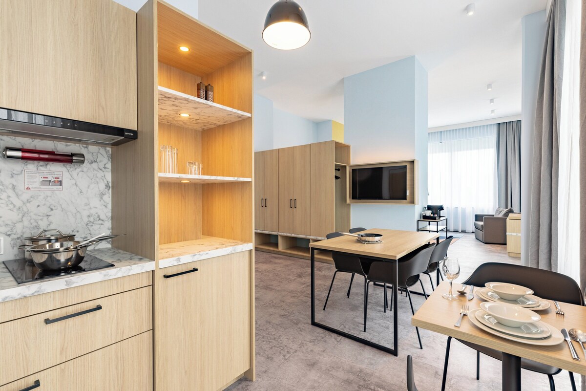 A modern kitchen with wooden cabinets, a built-in stove, and a dining area with a table and chairs.