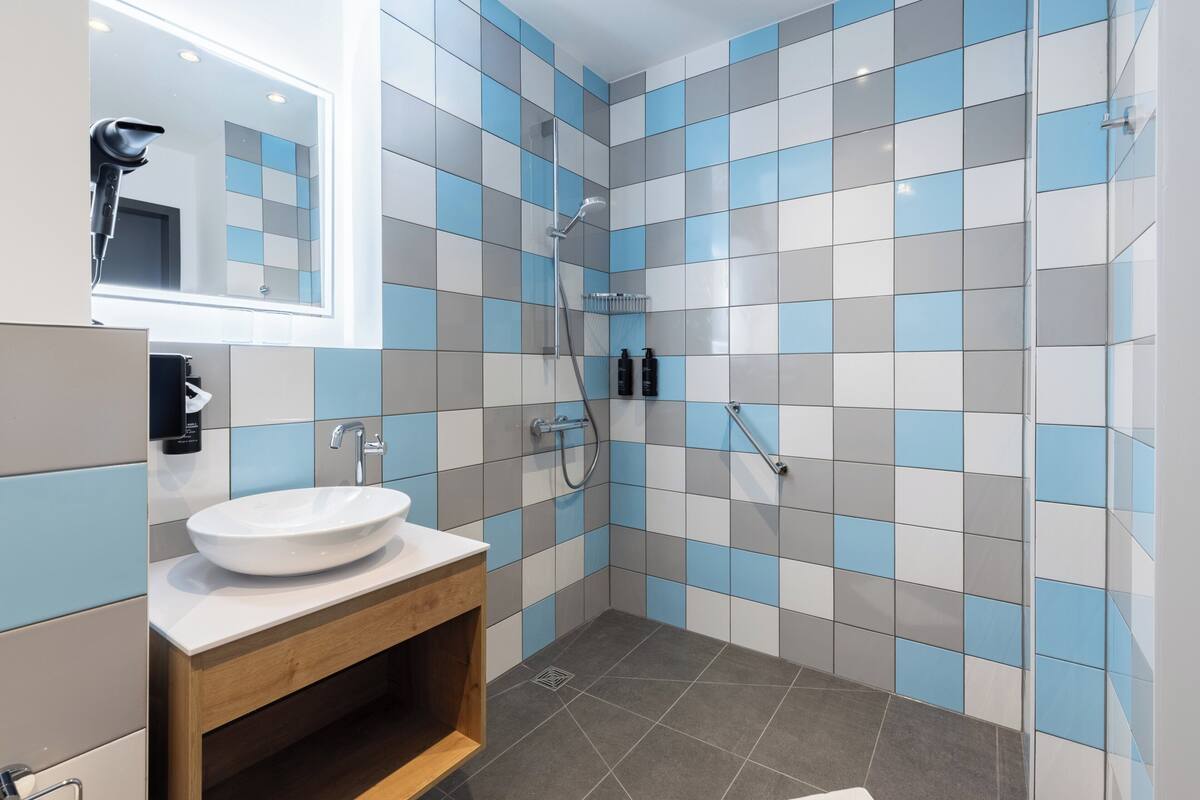 A modern bathroom with a white sink, a mirror, a handheld showerhead, and a tiled shower wall.
