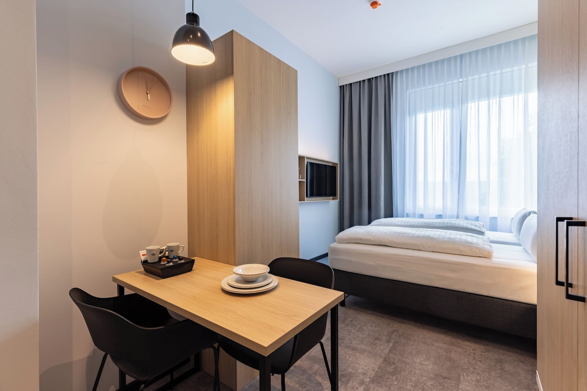 Hotelkamer met een bed, een televisie, een bureau met stoelen, een klok en een raam met gordijnen.