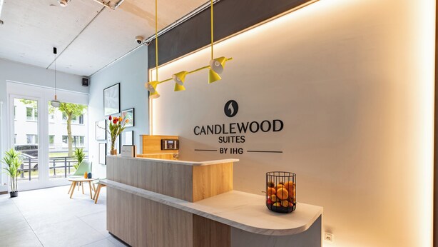 A reception desk with a sign for Candlewood Suites by IHG, a plant, and a fruit basket.