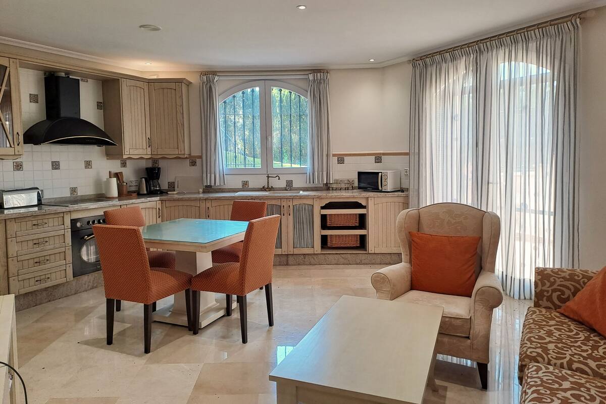 A modern kitchen with a dining area, featuring a large window, wooden cabinets, and a built-in oven.