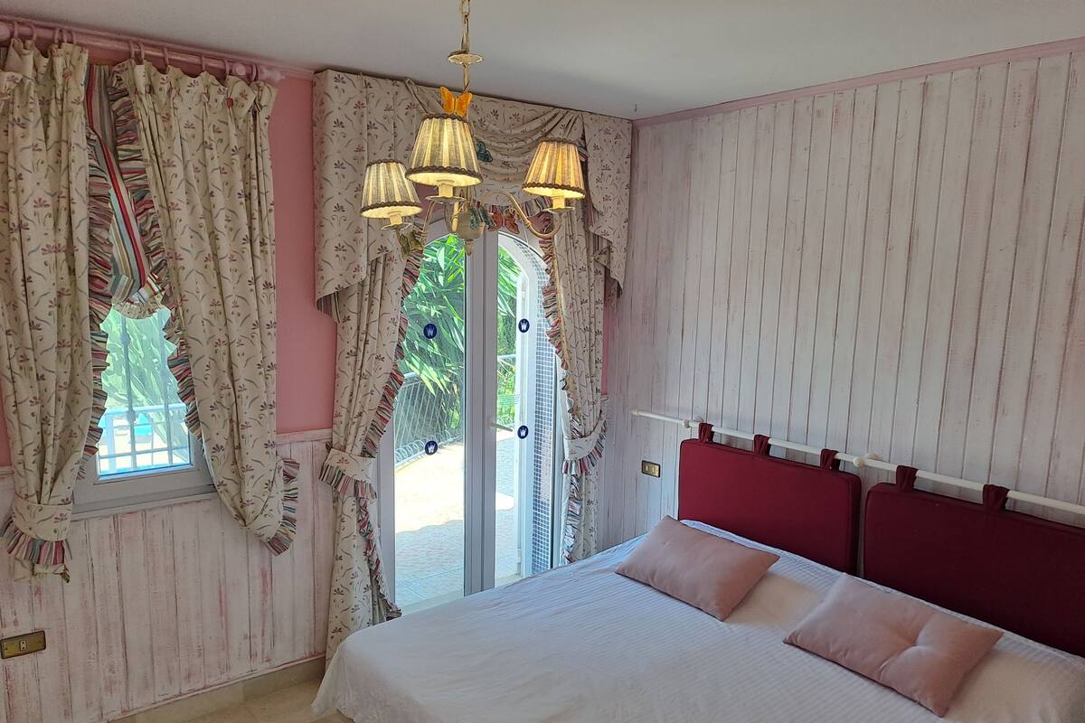 A bedroom with a bed, curtains, a window, and a wall with a striped pattern.