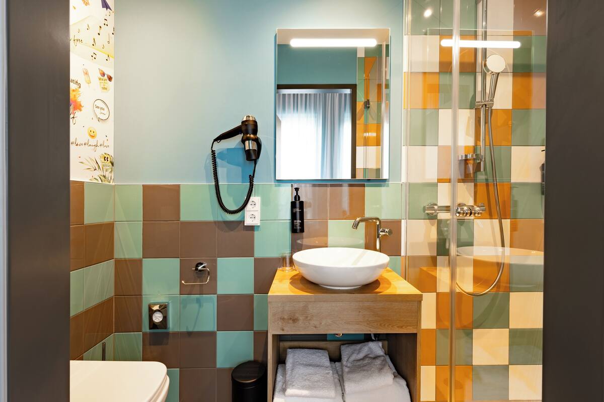 A bathroom with a white sink, a mirror, a hairdryer, and a shower.