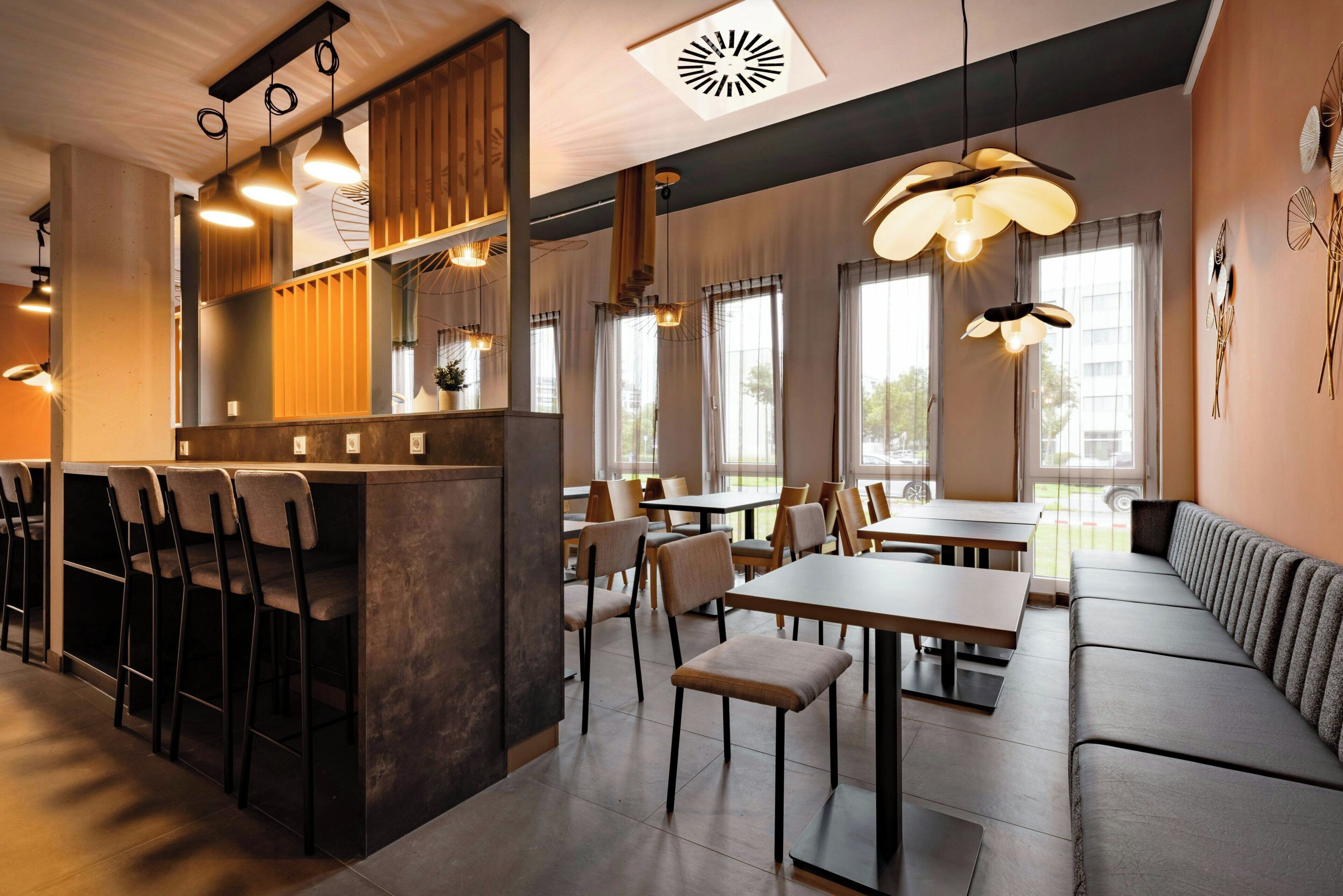 A modern restaurant interior with a bar area, seating arrangements, and pendant lighting.
