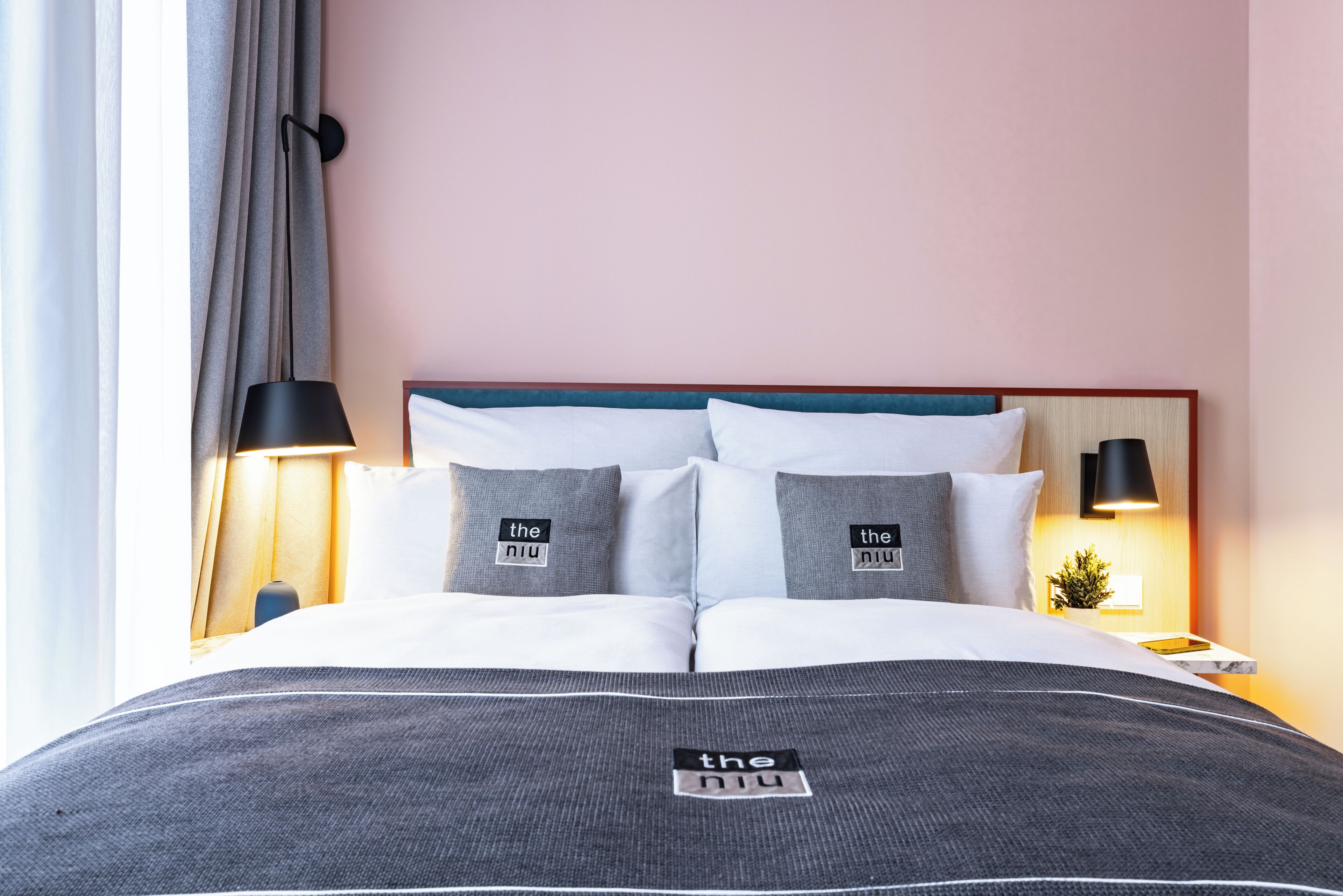 A neatly made bed with a grey bedspread and pillows, a wooden headboard, and a bedside table with a lamp.