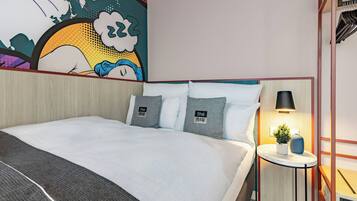 Una habitación de hotel moderna con una cama grande, una mesita de noche con lámpara y un mural colorido en la pared.