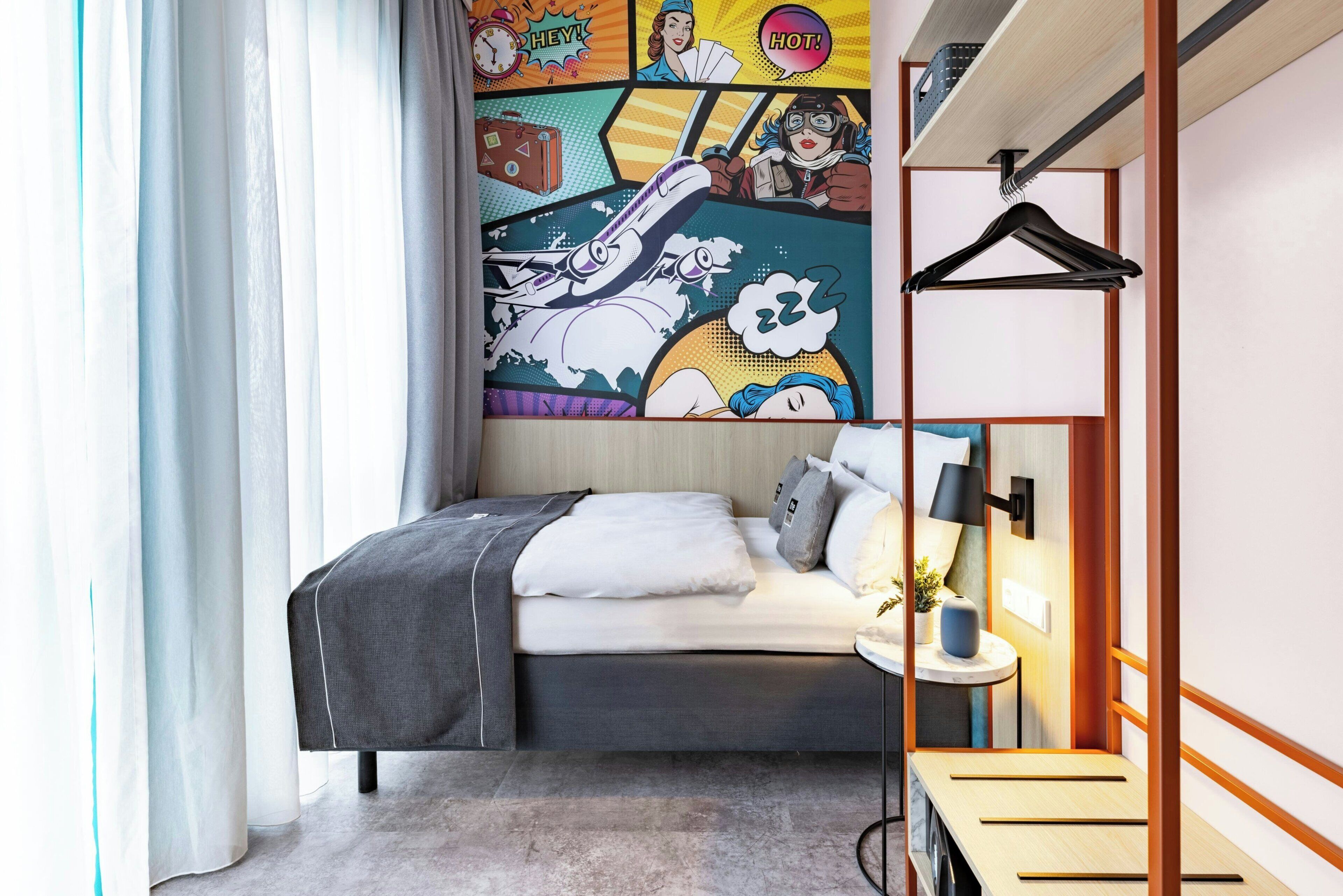 Un dormitorio moderno con cama, mesita de noche, lámpara y un mural de pared de estilo cómic y colores vivos.