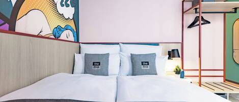 Habitación de hotel con cama, almohadas, una obra de arte en la pared, estante con planta y perchero.