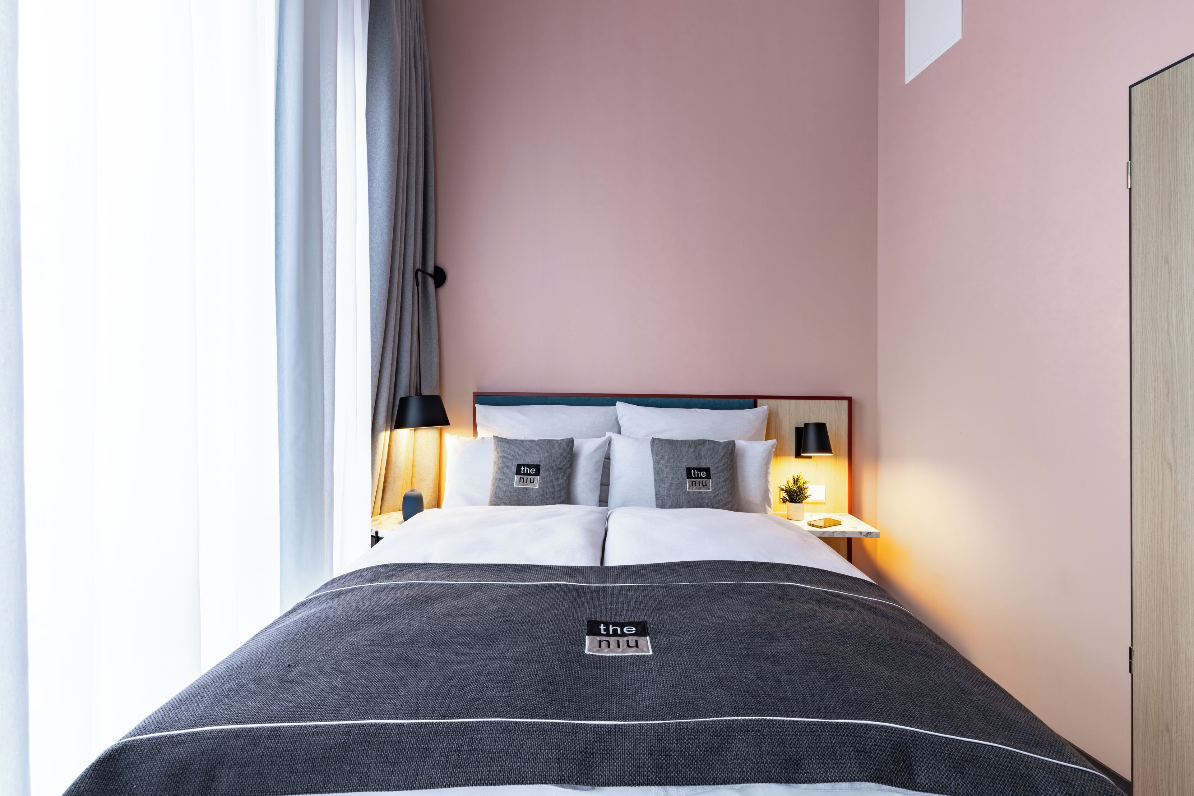 A hotel room with a bed, bedside lamps, a nightstand, and a window with curtains.