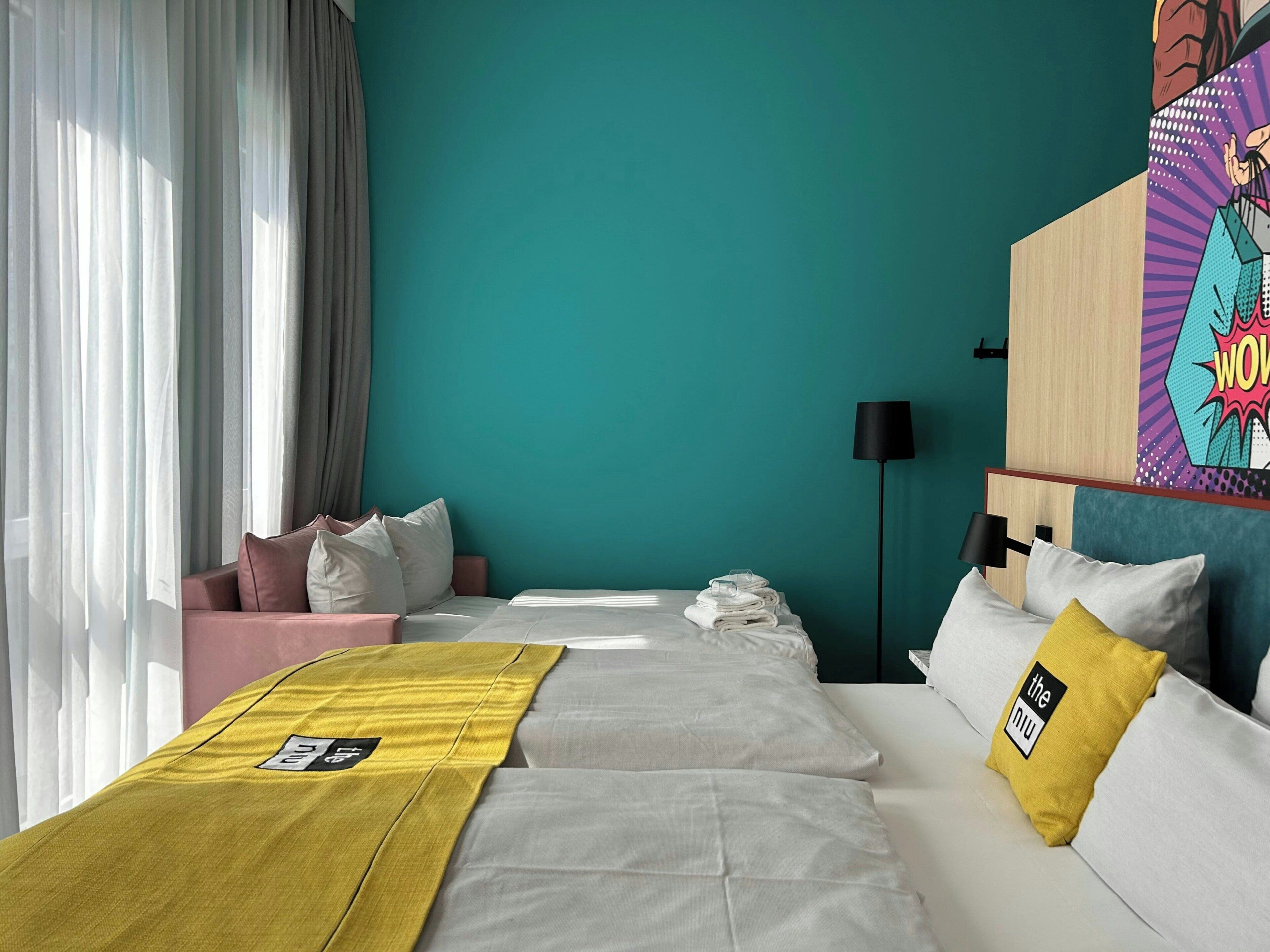 A hotel room with a bed, a sofa, a bedside table, a lamp, and a painting on the wall.