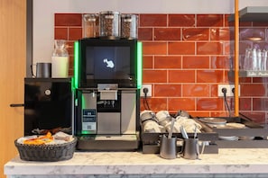 Een koffieapparaat met digitaal scherm, een koffiemolen en een mandje koffiepads op een marmeren aanrecht.