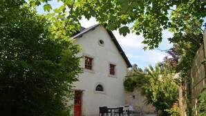 A white building with red doors and windows, surrounded by greenery and a small patio area with outdoor furniture. - The Manoir de Damigny in Normandy near the landing beaches and Bayeux (SAINT MARTIN DES ENTREES)