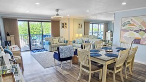 A spacious living area with a dining table, multiple chairs, a sofa, and a balcony with outdoor furniture. - Ocean Block, Ocean View 2 Bedroom Condo on 37th St. Sovereign Sea. Next to Coconuts Beach Bar and many other great places! Sovereign Sea #106 (Ocean City)