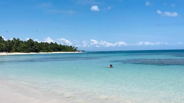 Una playa con agua turquesa cristalina, una orilla arenosa y una persona nadando.