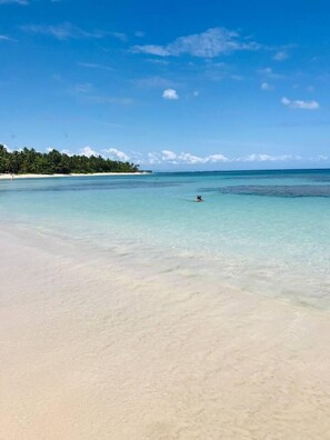 A beach with clear turquoise water, a sandy shore, and a person swimming. - Piece of Paradise in Las Terrenas (Las Terrenas)