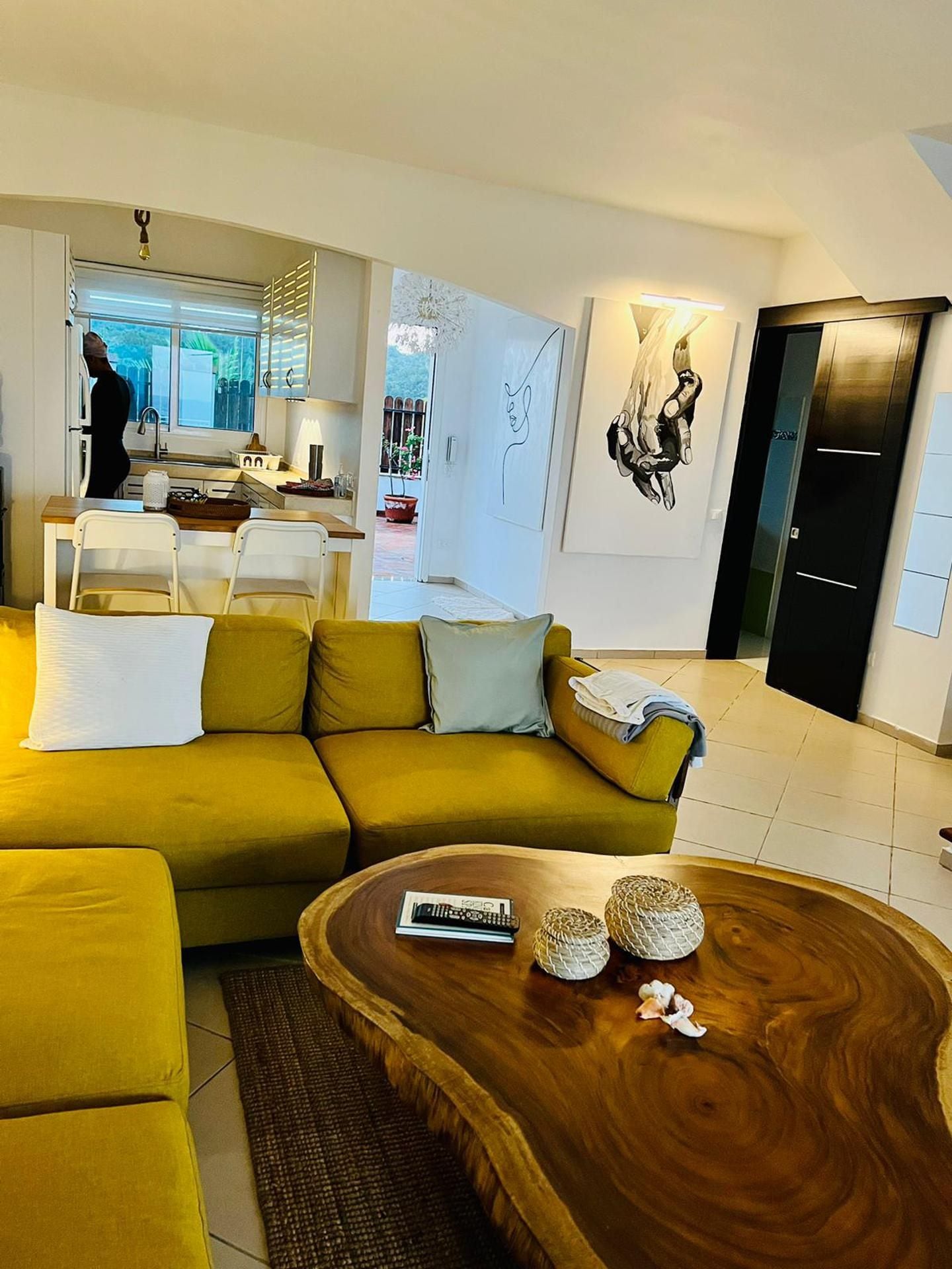 A modern living room with a yellow sofa, a wooden coffee table, and a kitchen in the background.