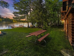 A lakeside cabin with a picnic table, dock, and chairs.