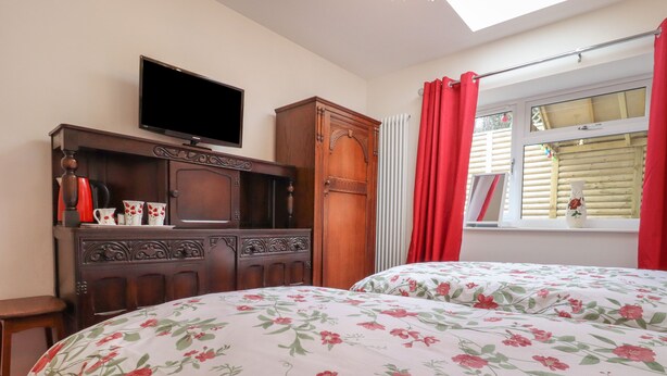 Une chambre avec deux lits, un téléviseur posé sur un meuble en bois et une fenêtre ornée de rideaux rouges.